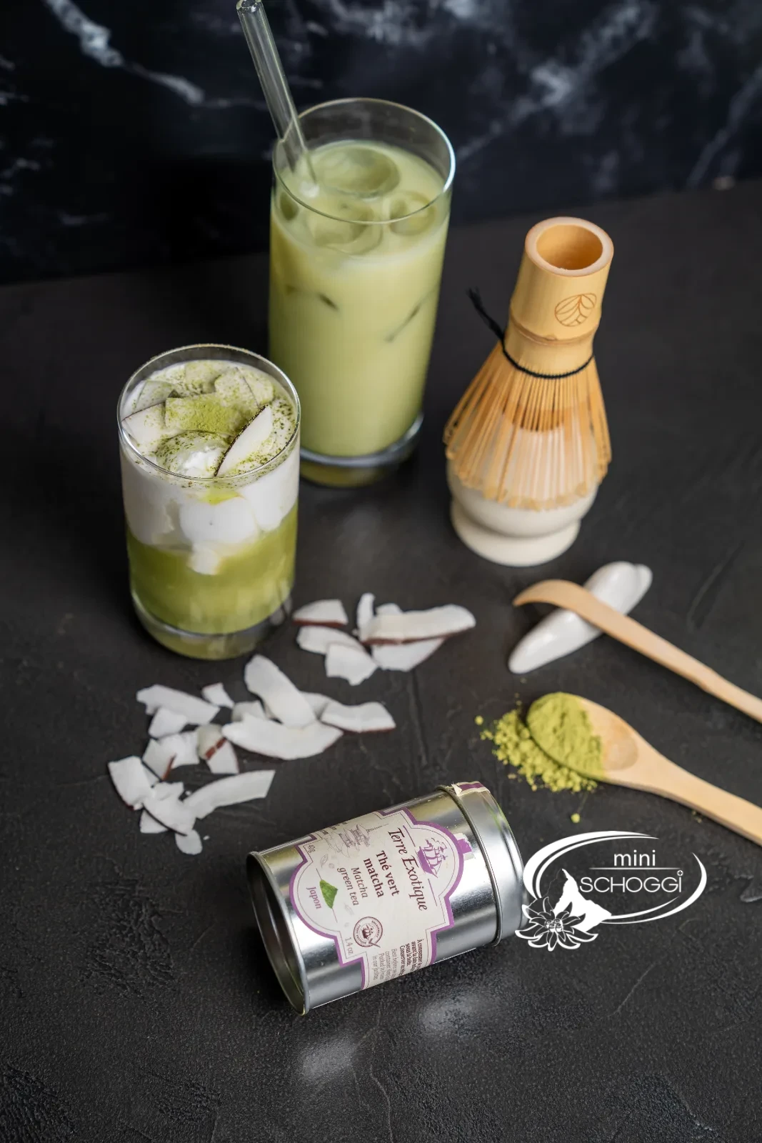 Three glasses of matcha iced latte with a matcha tin and bamboo whisk on marble