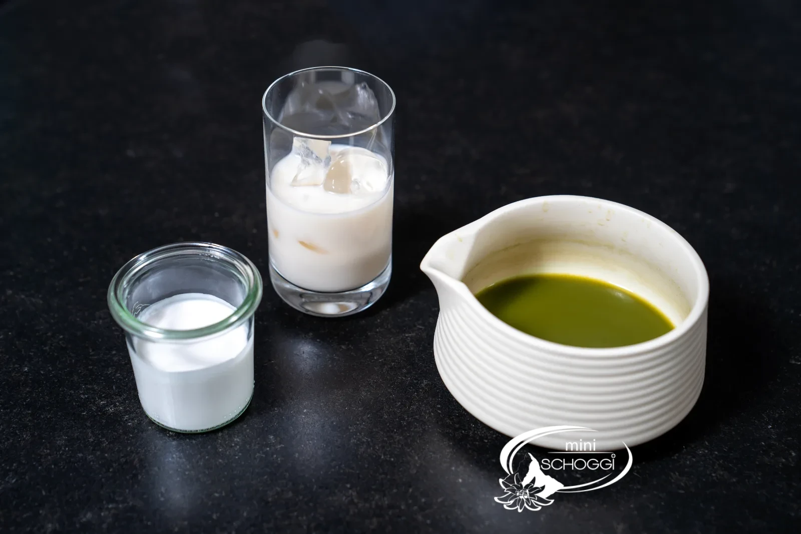 Glass with ice cubes and milk next to the bowl of whisked matcha