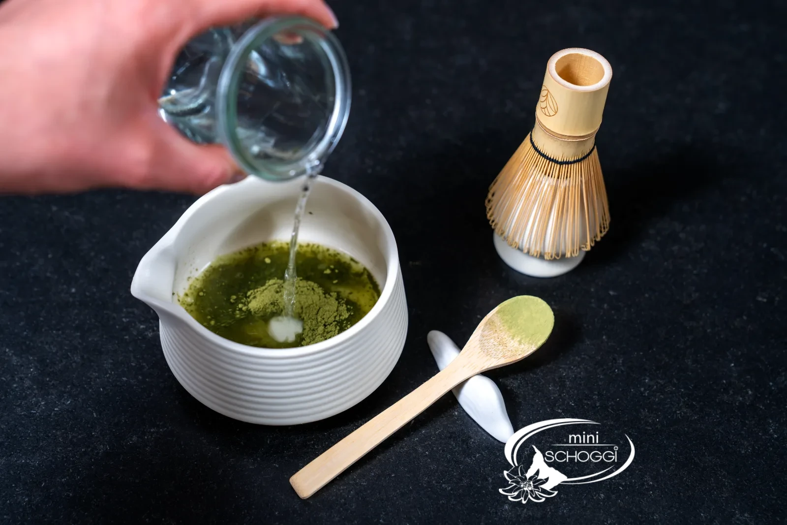 Sieved matcha powder in the bowl, next to a glass of hot water