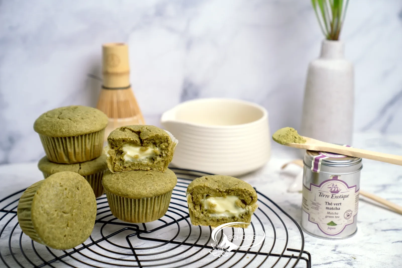 Matcha Muffins mit cremigem Frischkäsekern auf dem Kuchengitter, dazu Matcha-Dose und Bambusbesen