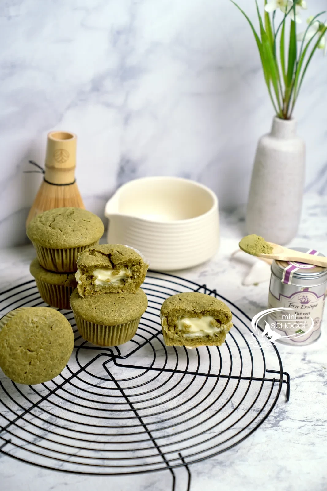 Matcha Muffins mit cremigem Frischkäsekern auf dem Kuchengitter, dazu Matcha-Dose und Bambusbesen