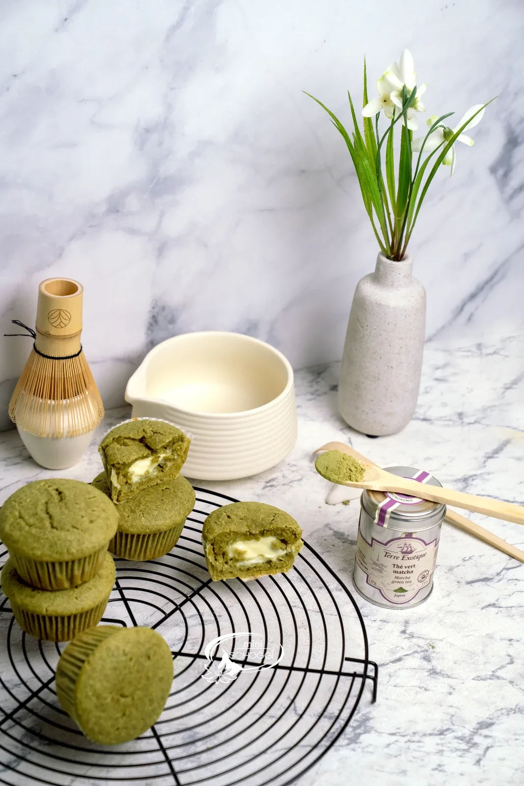 Matcha Muffins mit cremigem Frischkäsekern auf dem Kuchengitter, dazu Matcha-Dose und Bambusbesen