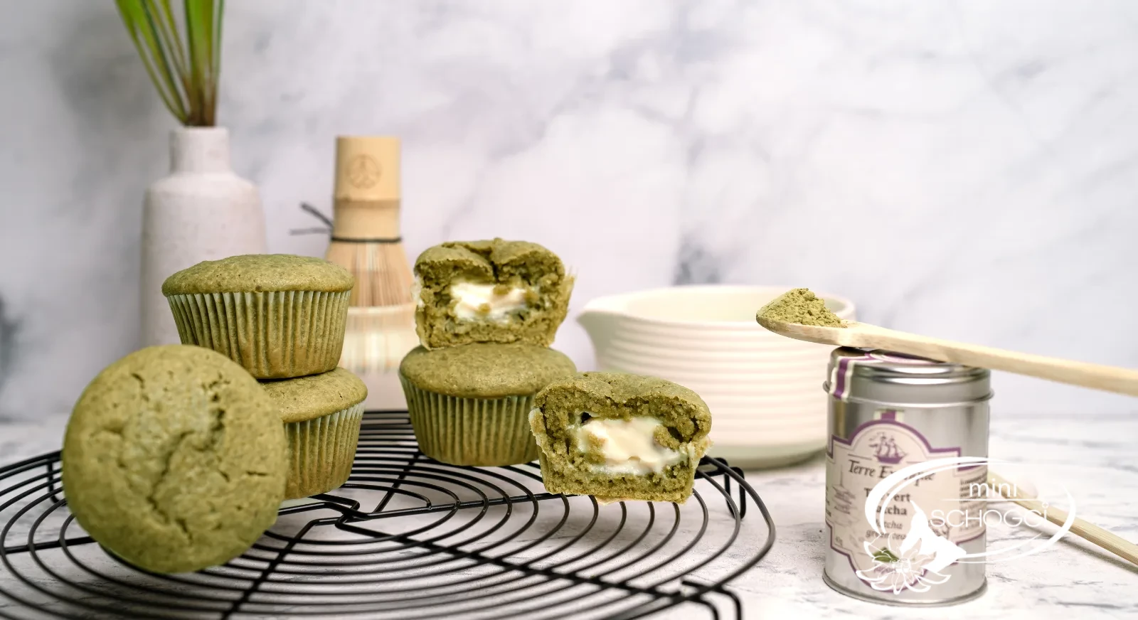 Matcha Muffins mit cremigem Frischkäsekern auf dem Kuchengitter, dazu Matcha-Dose und Bambusbesen