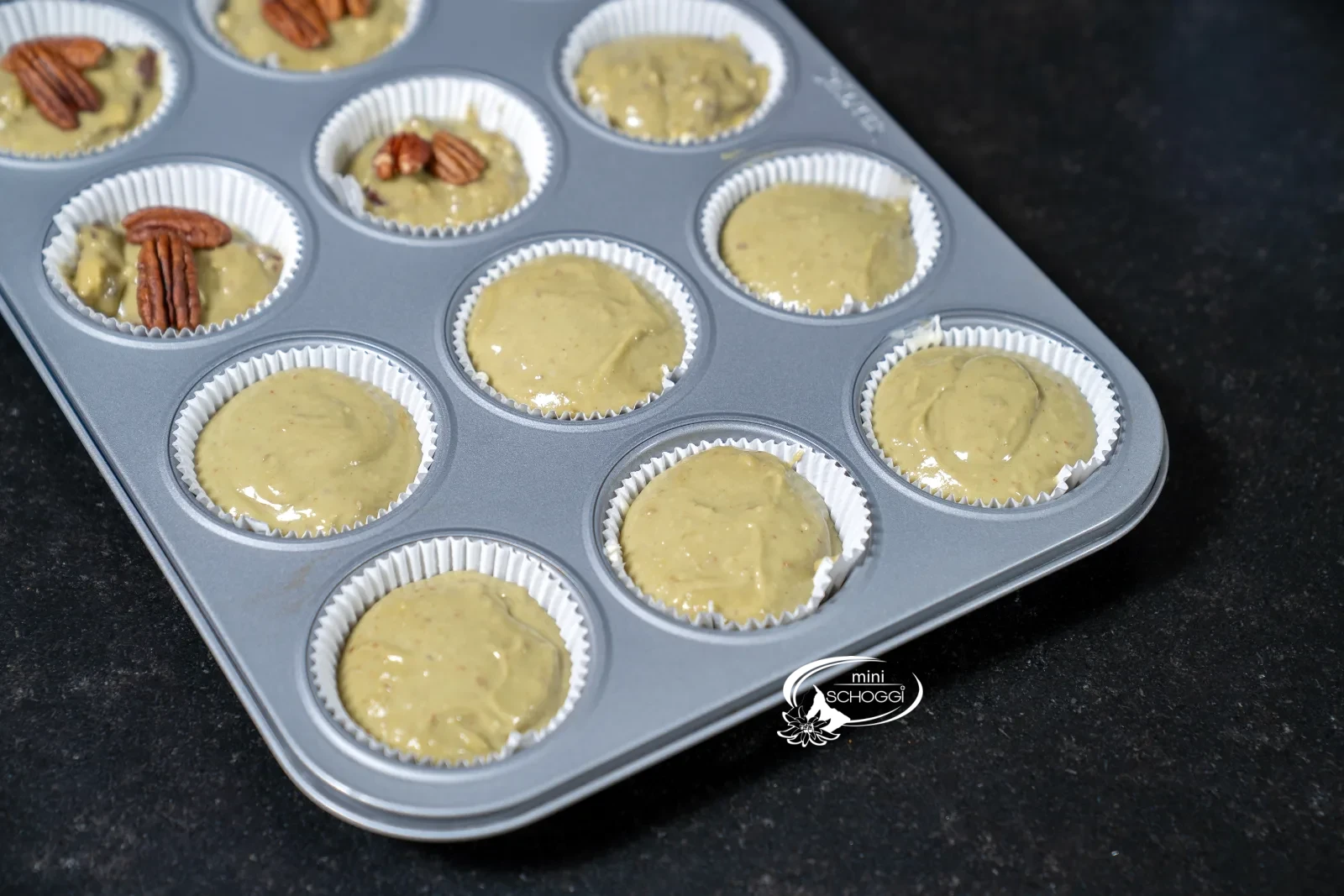 Die Frischkäsecreme ist mit Matcha-Teig abgedeckt, die Förmchen sind bereit zum Backen