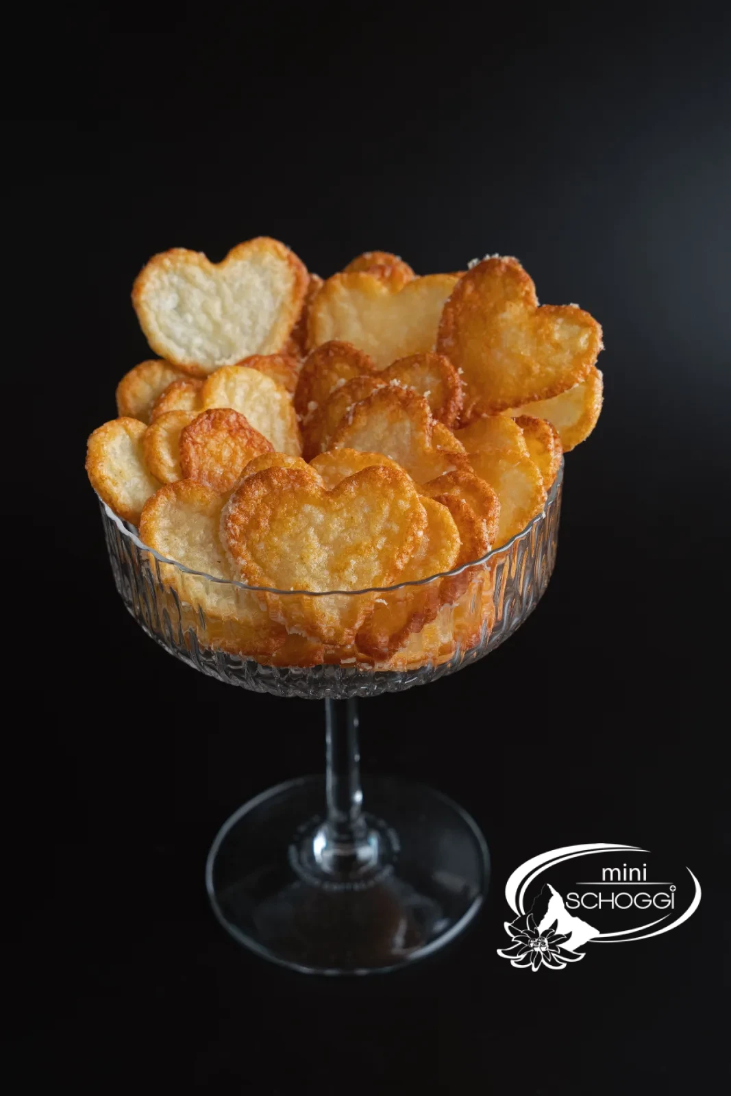 Chips di parmigiano in una ciotola di vetro e confezionate in un sacchetto regalo, accanto un pezzo di parmigiano
