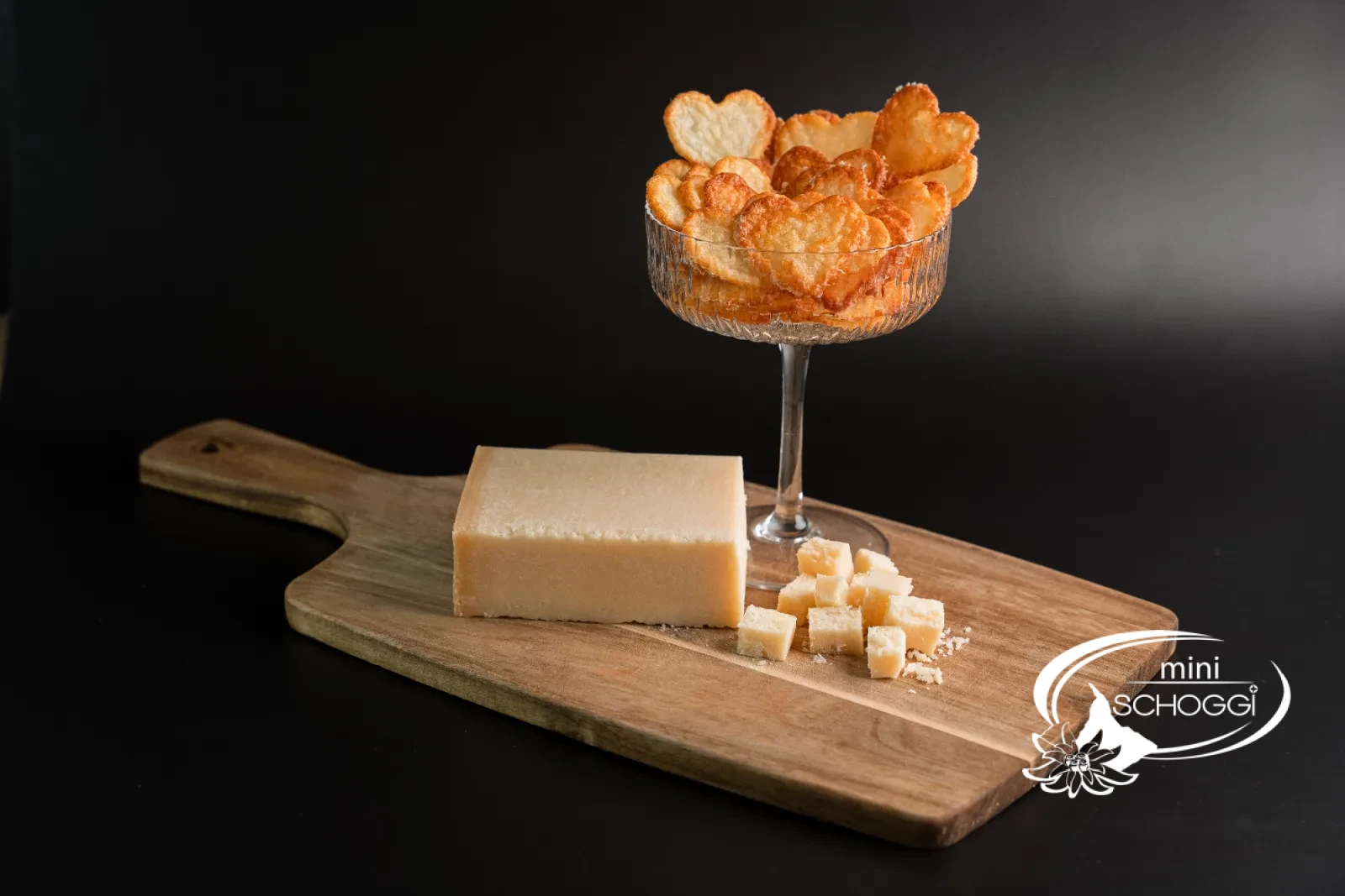 Chips di parmigiano in una ciotola di vetro e confezionate in un sacchetto regalo, accanto un pezzo di parmigiano