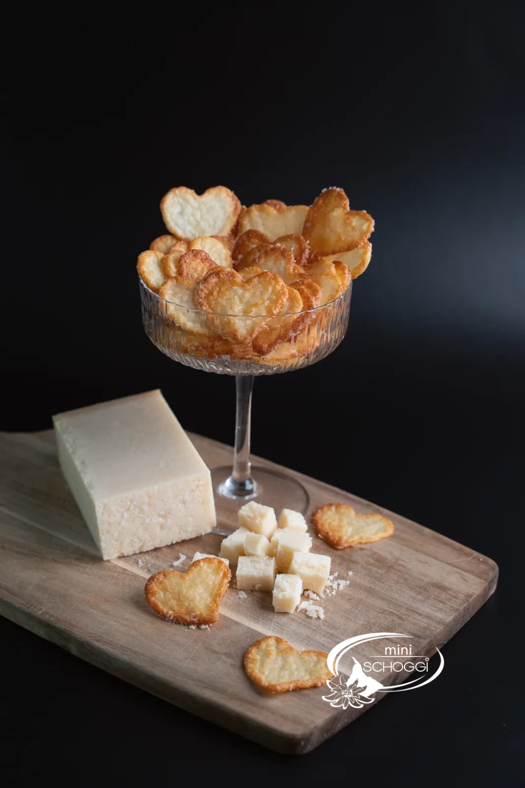 Chips di parmigiano in una ciotola di vetro e confezionate in un sacchetto regalo, accanto un pezzo di parmigiano