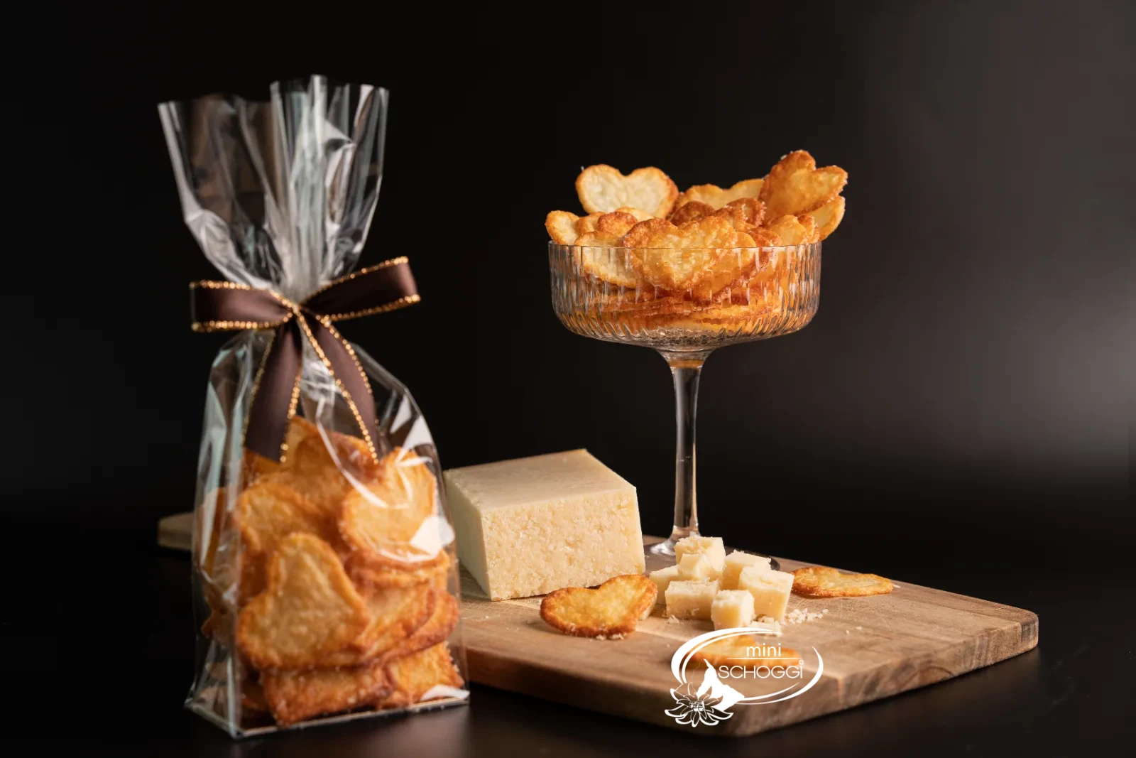 Chips di parmigiano in una ciotola di vetro e confezionate in un sacchetto regalo, accanto un pezzo di parmigiano