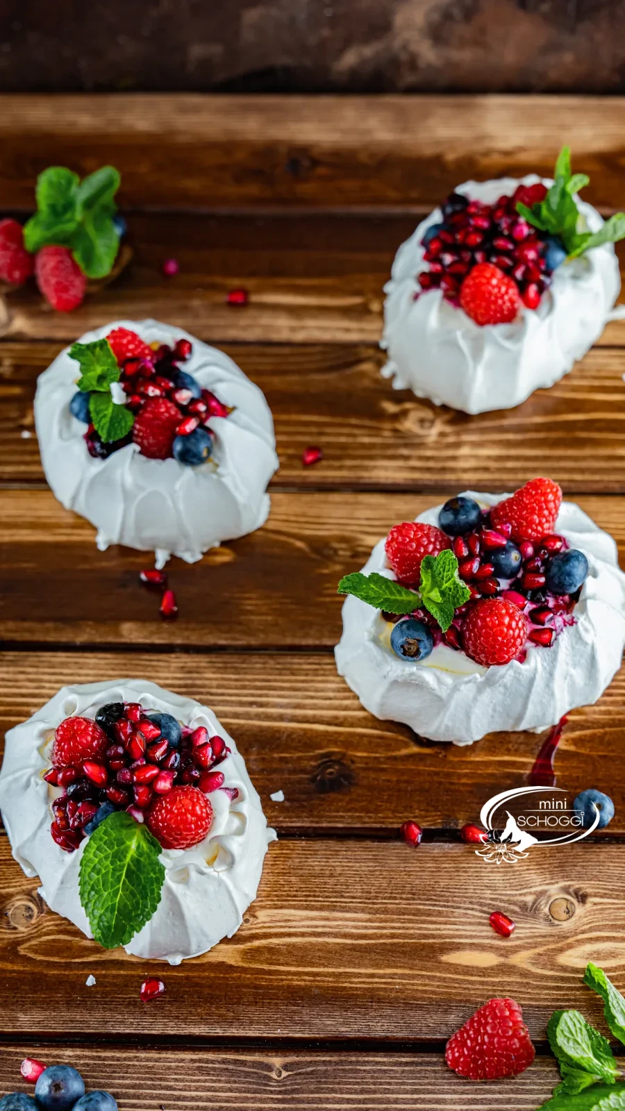 Nids de pavlova avec crème, framboises, myrtilles et graines de grenade sur bois foncé