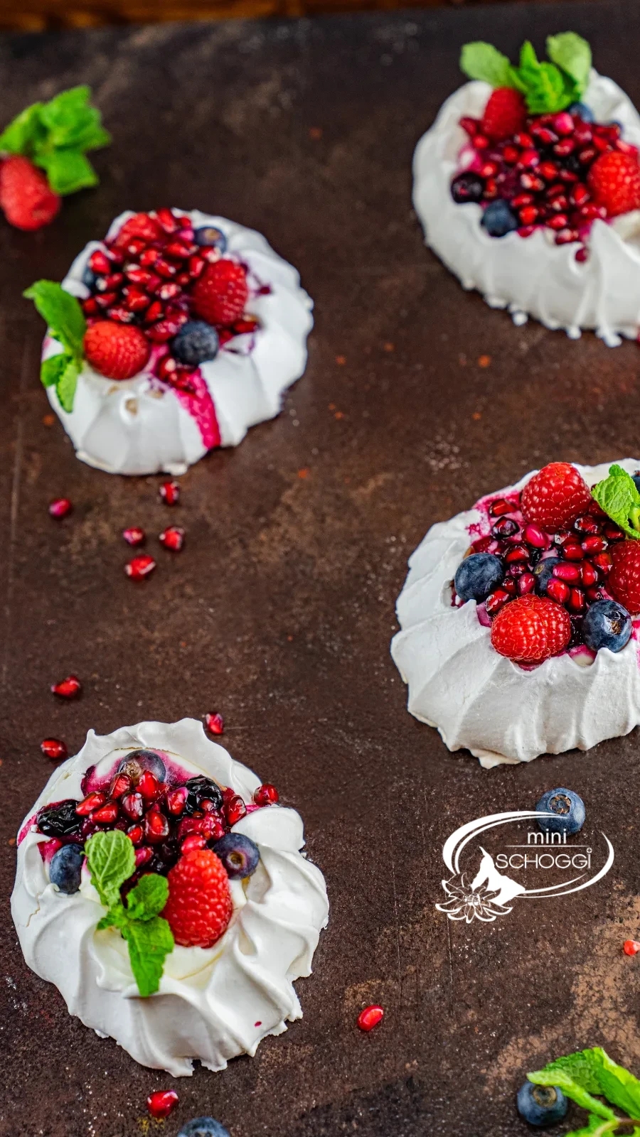 Nids de pavlova avec crème, framboises, myrtilles et grains de grenade sur bois foncé