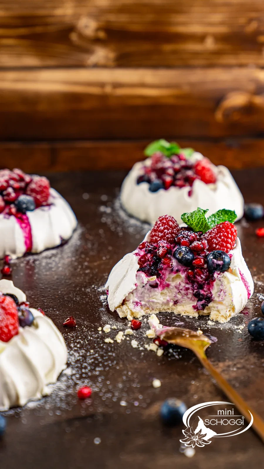 Nids de pavlova avec crème, framboises, myrtilles et grains de grenade sur bois foncé