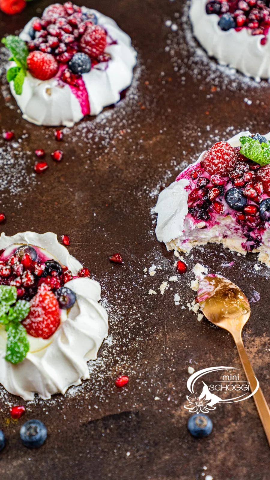 Nids de pavlova avec crème, framboises, myrtilles et grains de grenade sur bois foncé