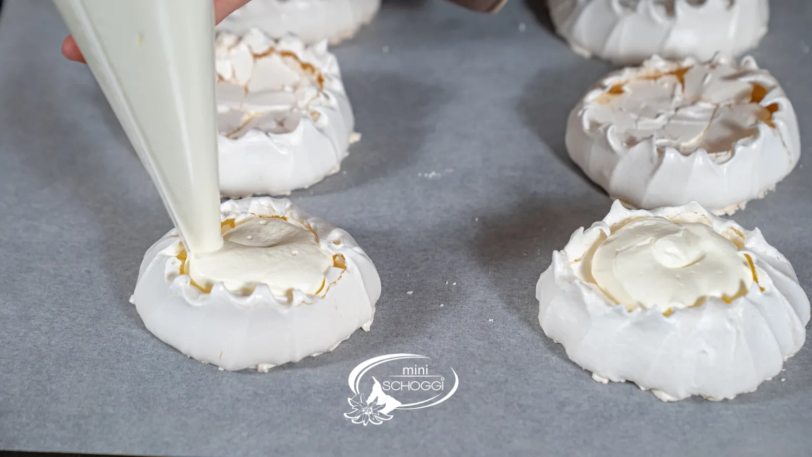 De la crème fouettée est déposée depuis la poche à douille dans le nid de meringue