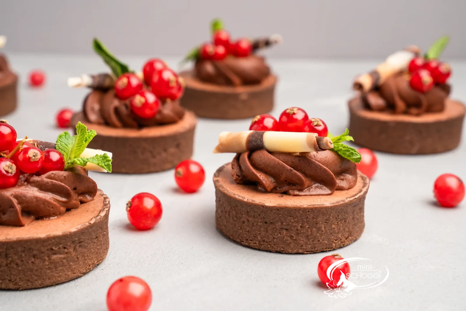 Tortino al cioccolato con rosette di mousse, ribes e menta su un tavolo chiaro