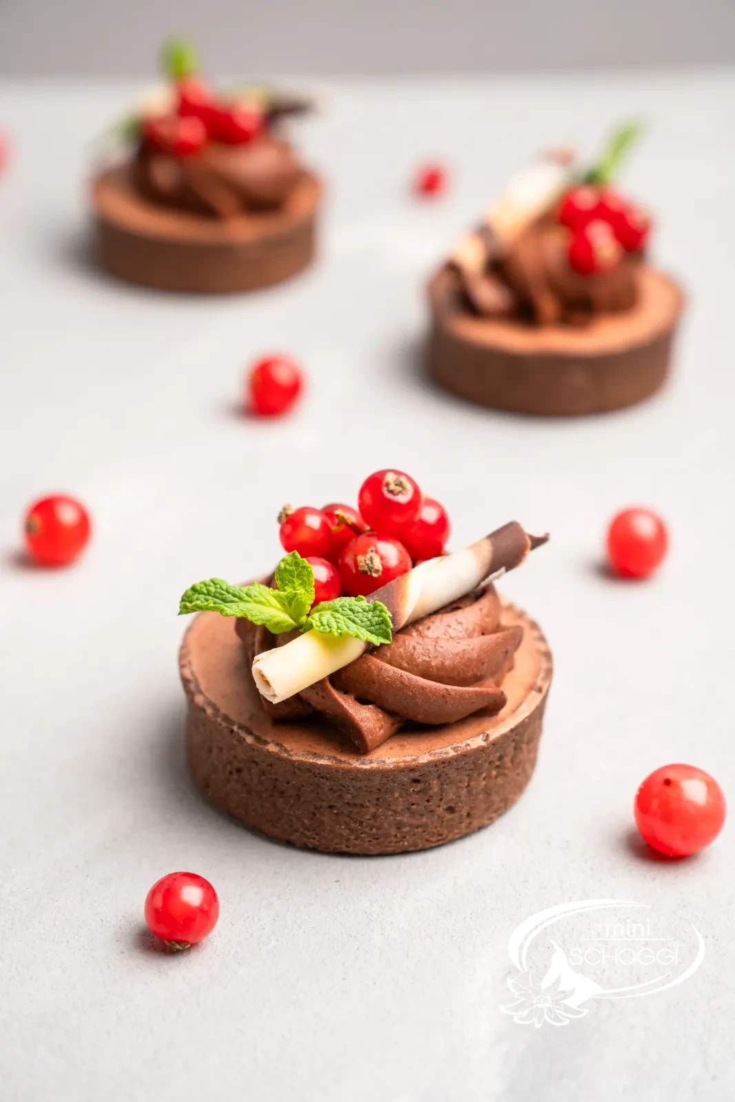 Tortino al cioccolato con rosette di mousse, ribes e menta su un tavolo chiaro