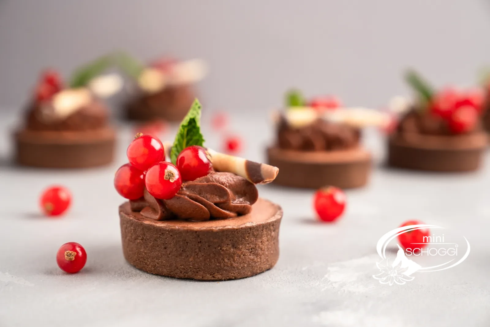 Tortino al cioccolato con rosette di mousse, ribes e menta su un tavolo chiaro