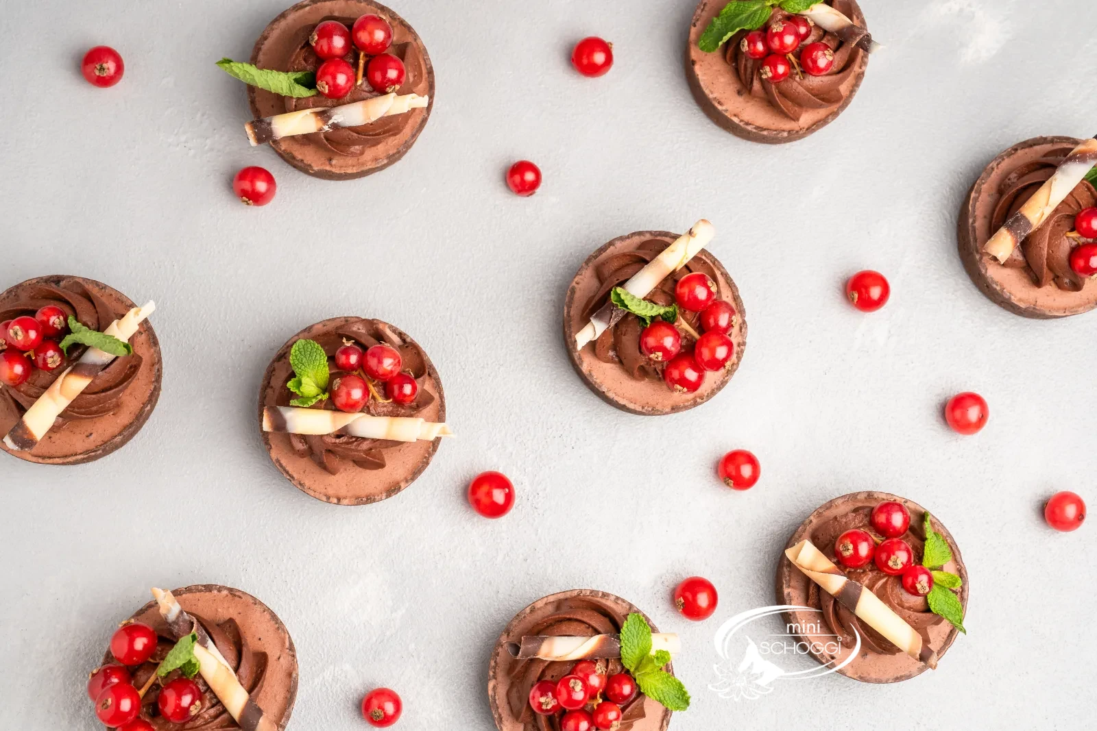 Tortino al cioccolato con rosette di mousse, ribes e menta su un tavolo chiaro