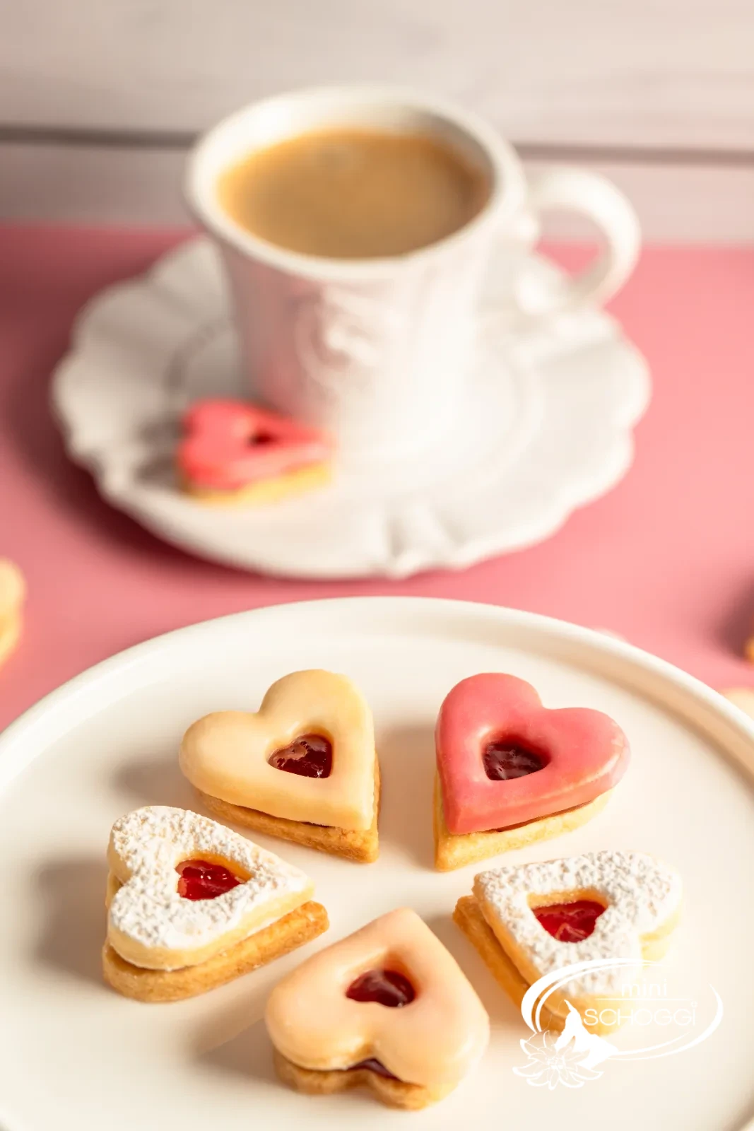 Cuori occhi di bue con glassa rosa e confettura accanto a una tazza di caffè