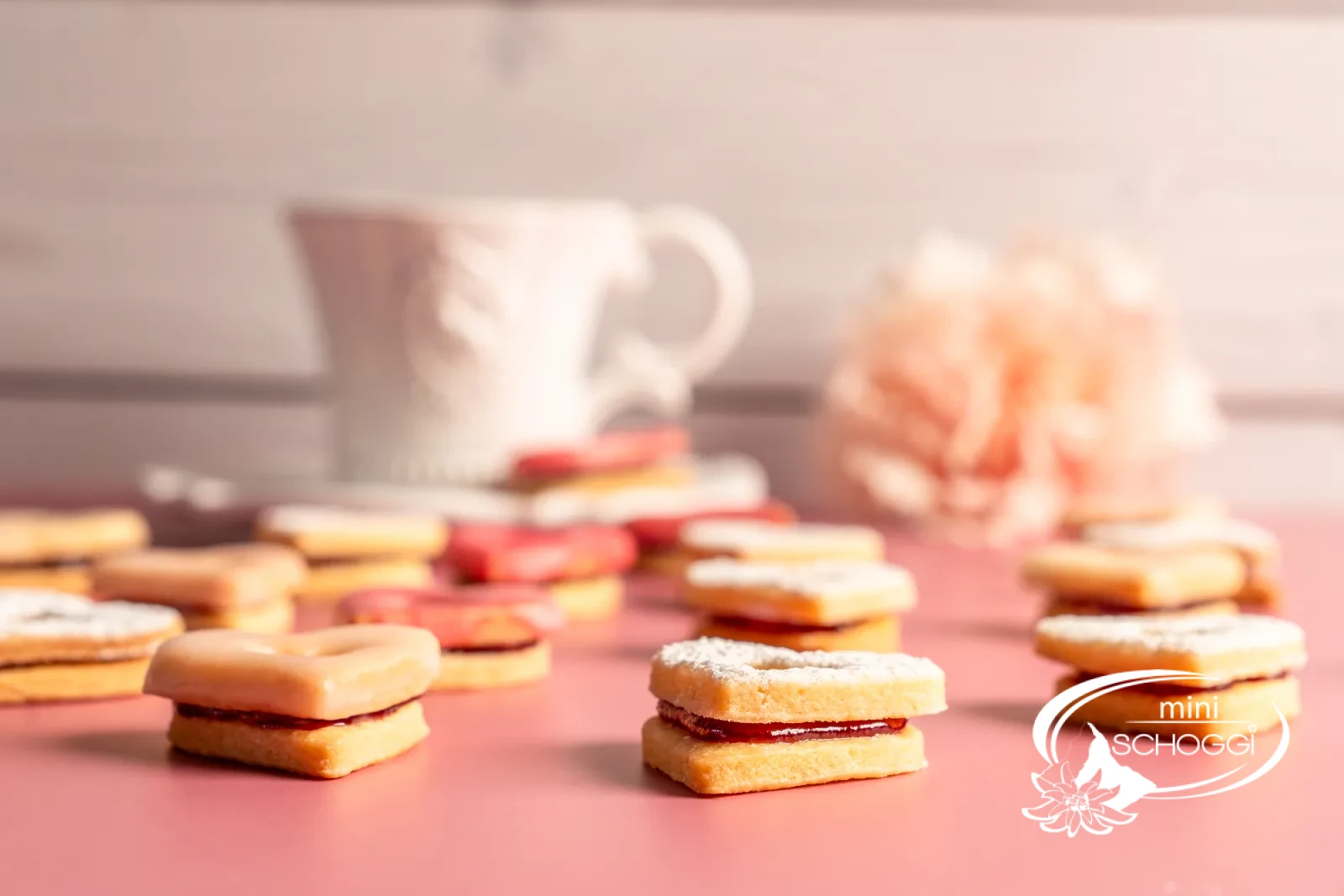 Cuori occhi di bue con glassa rosa e confettura accanto a una tazza di caffè