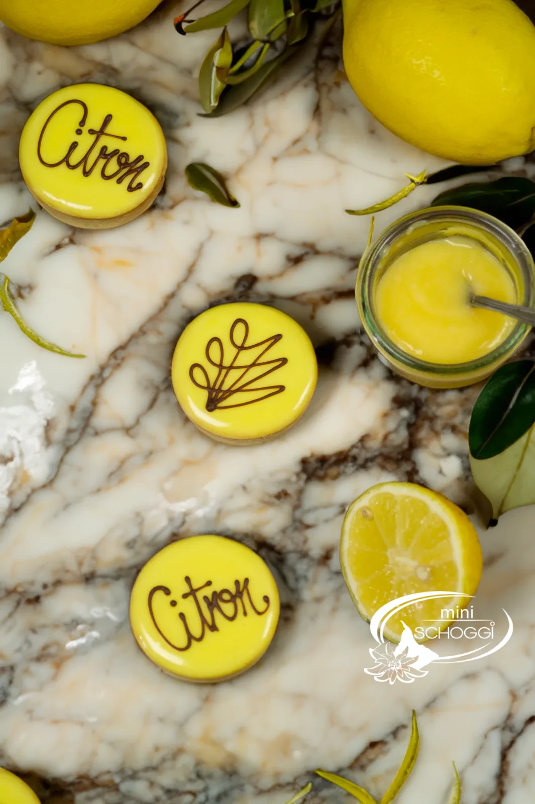 Crostatine al limone con glassa gialla di fondant e la scritta Citron accanto a limoni tagliati