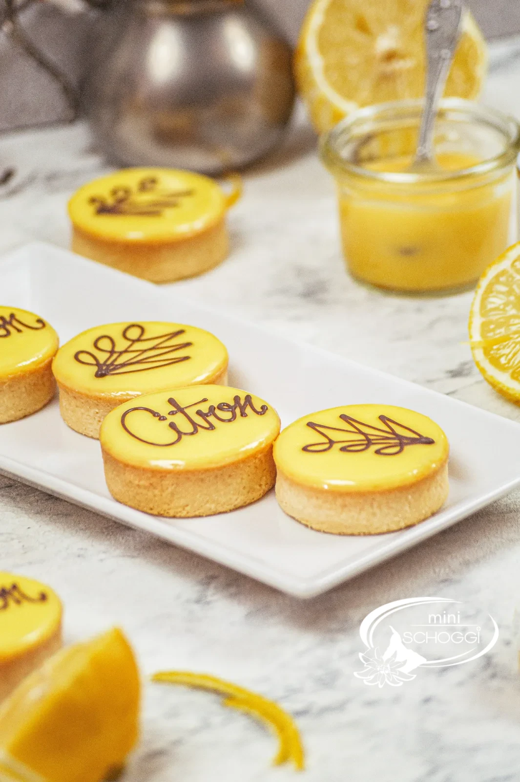 Crostatine al limone con glassa gialla di fondant e la scritta Citron accanto a limoni tagliati
