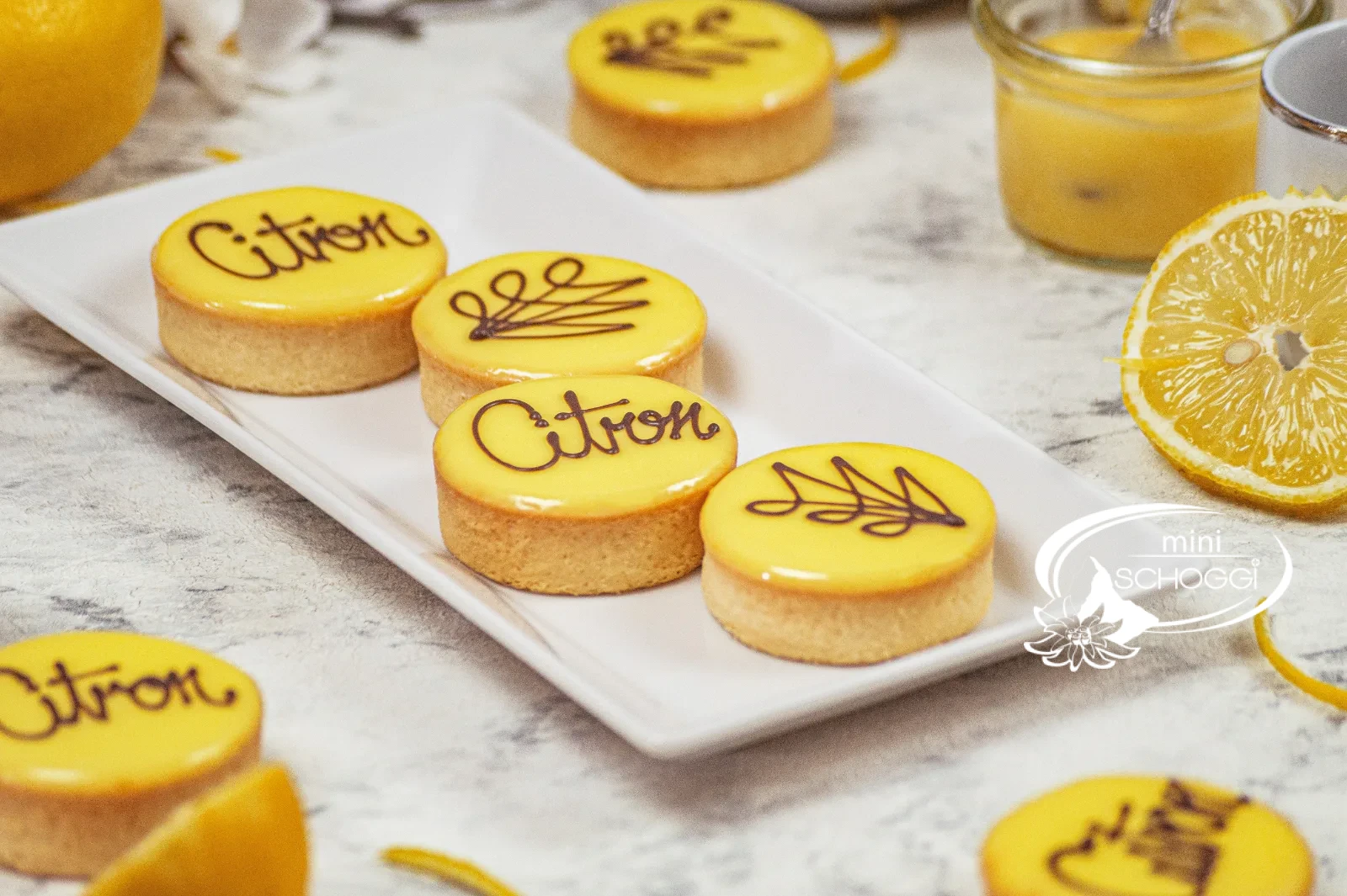 Tartelette al limone con glassa gialla al fondant e la scritta Citron accanto a limoni tagliati