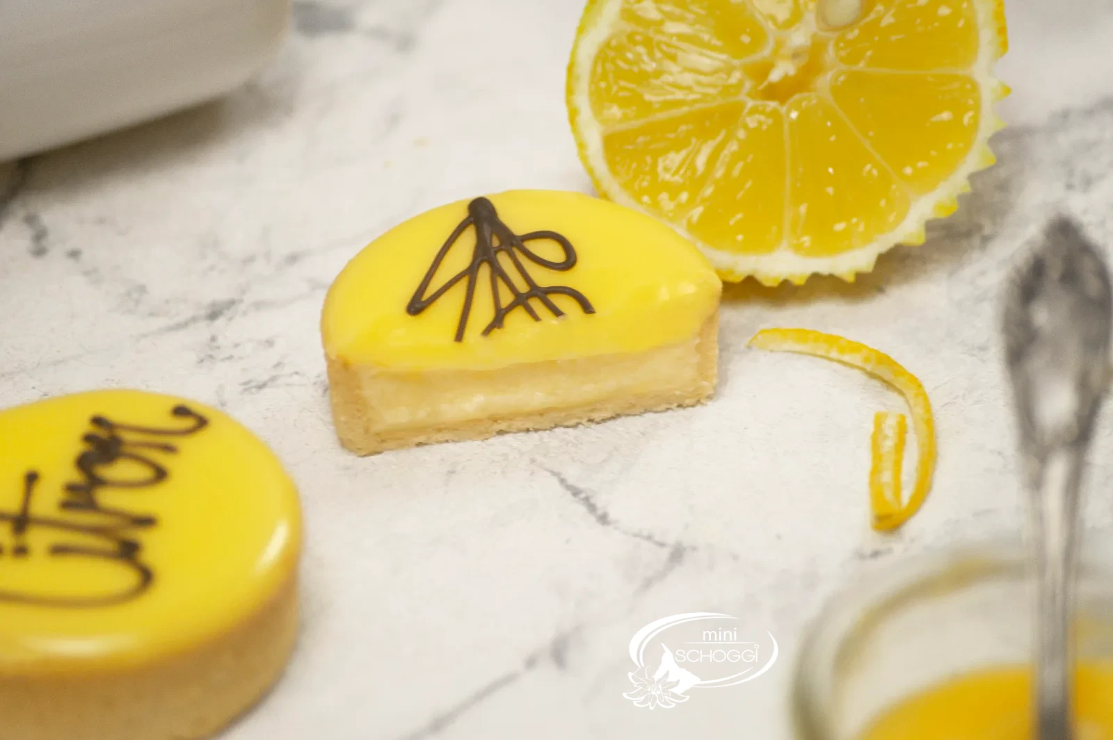 Crostatine al limone con glassa gialla di fondant e la scritta Citron accanto a limoni tagliati
