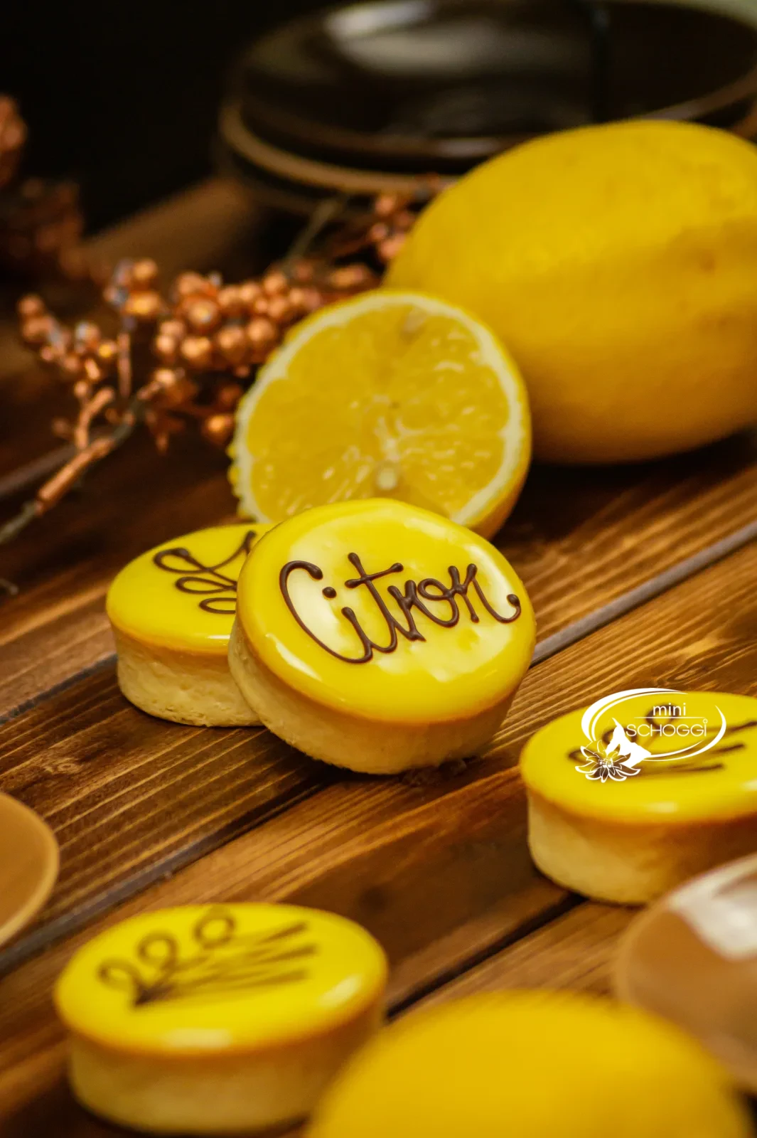 Tartelette al limone con glassa gialla di fondant e la scritta Citron accanto a limoni tagliati