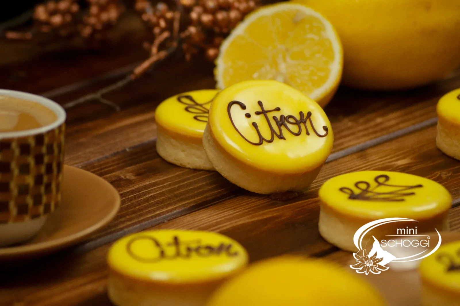 Crostatine al limone con glassa gialla di fondant e la scritta Citron accanto a limoni tagliati