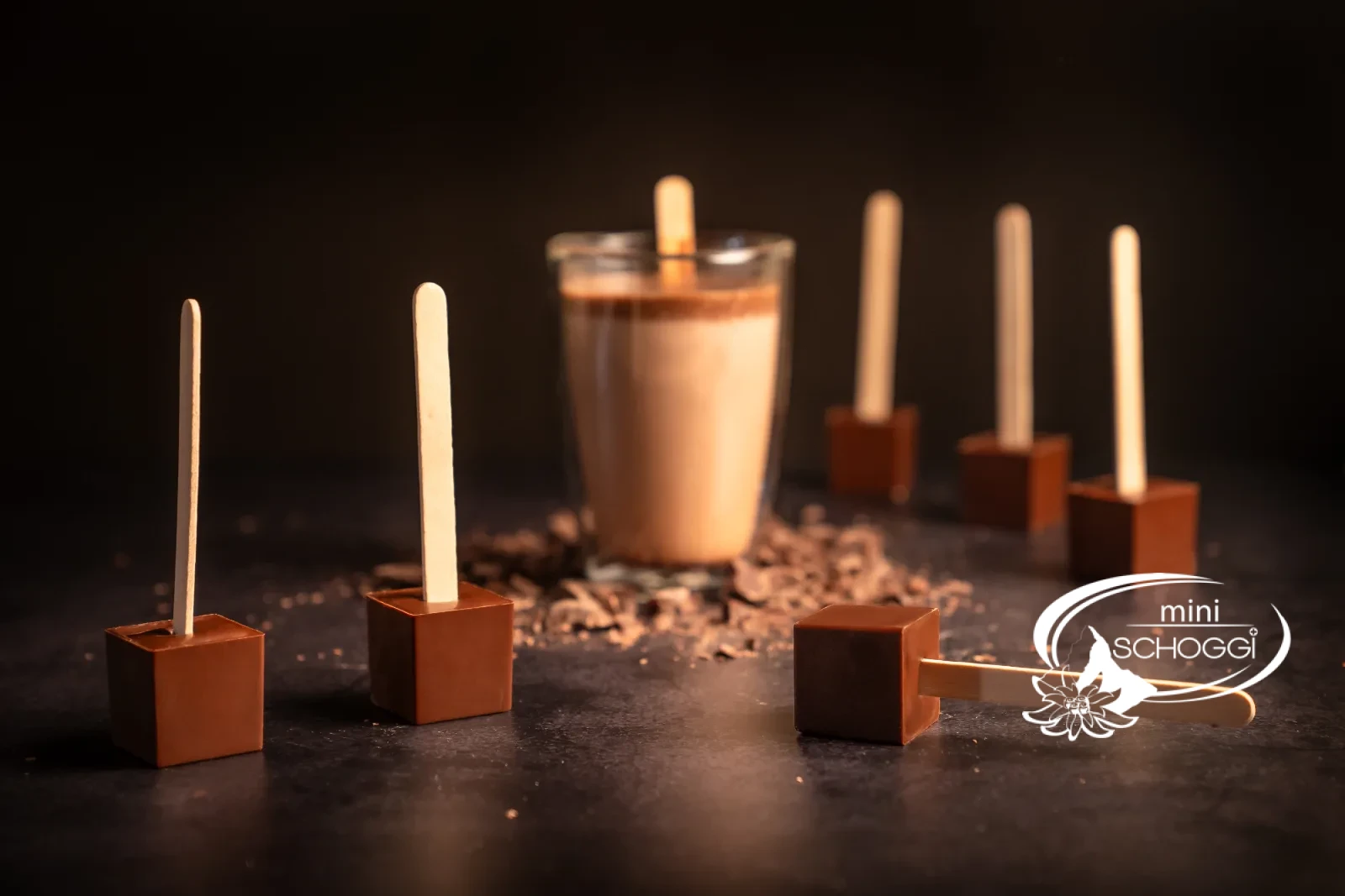 Ein Trinkschokoladen-Würfel am Stiel wird in eine Tasse heisse Milch getaucht