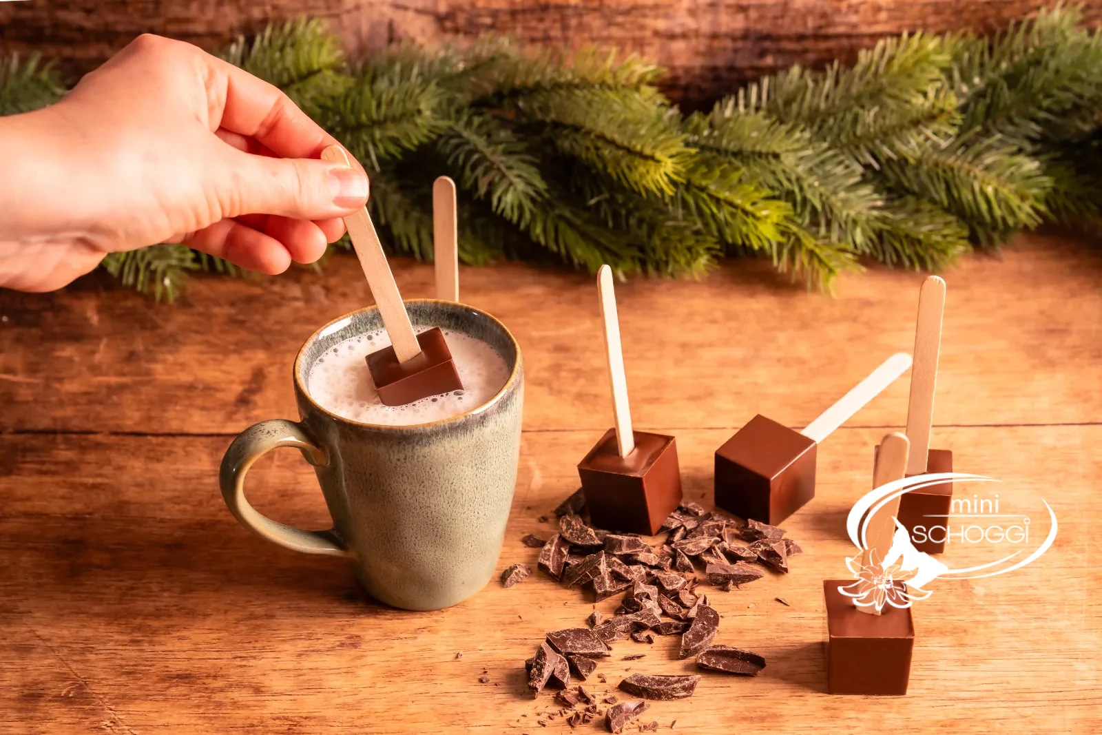 Ein Trinkschokoladen-Würfel am Stiel wird in eine Tasse heisse Milch getaucht