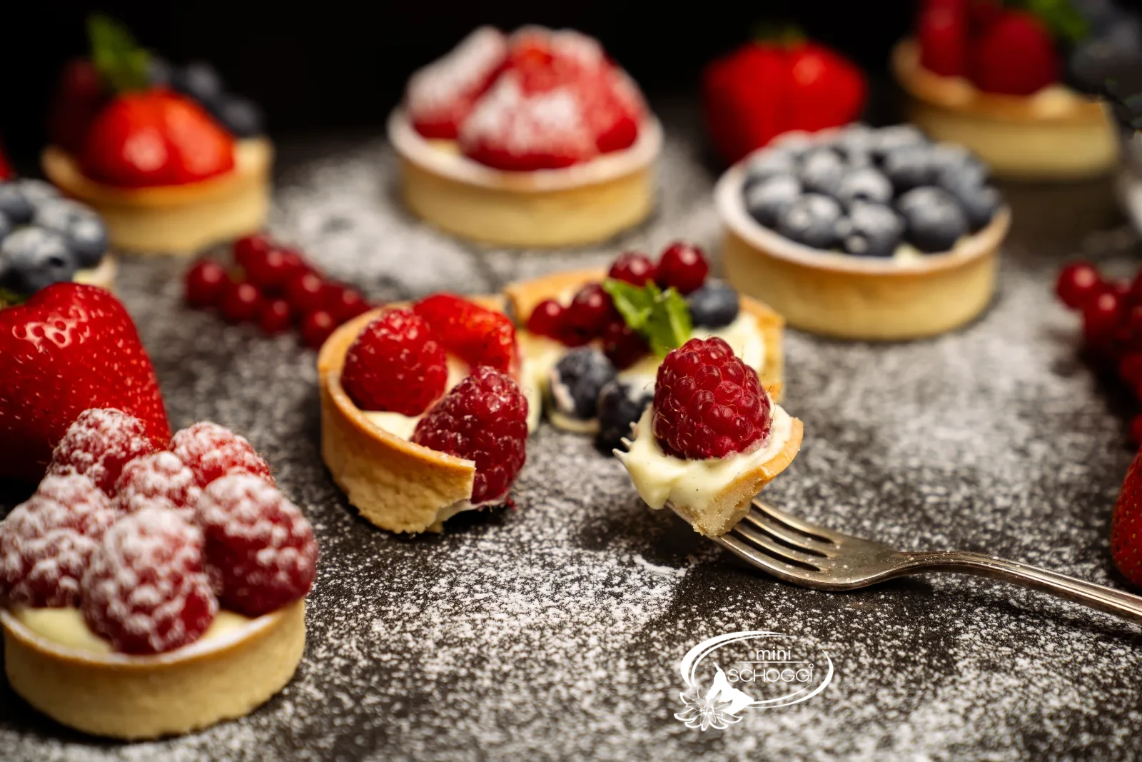 Fertige Vanillecreme-Törtchen mit frischen Beeren und Puderzucker