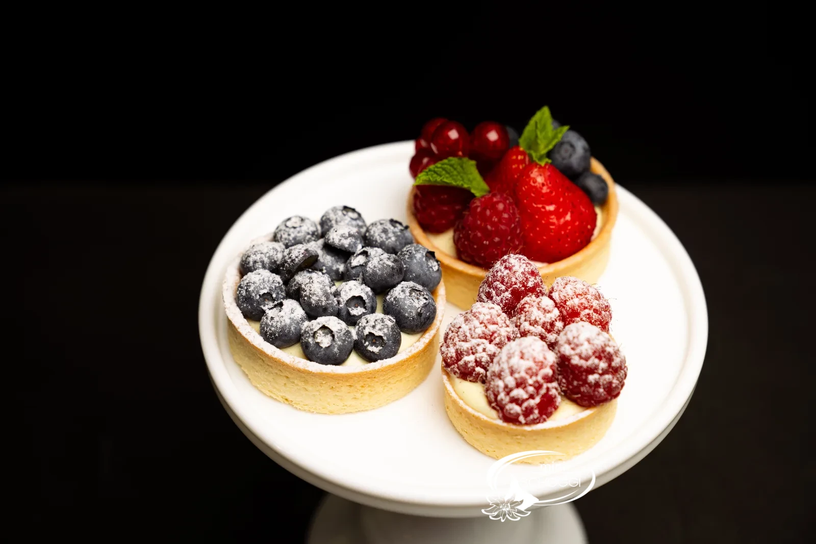 Fertige Vanillecreme-Törtchen mit frischen Beeren und Puderzucker