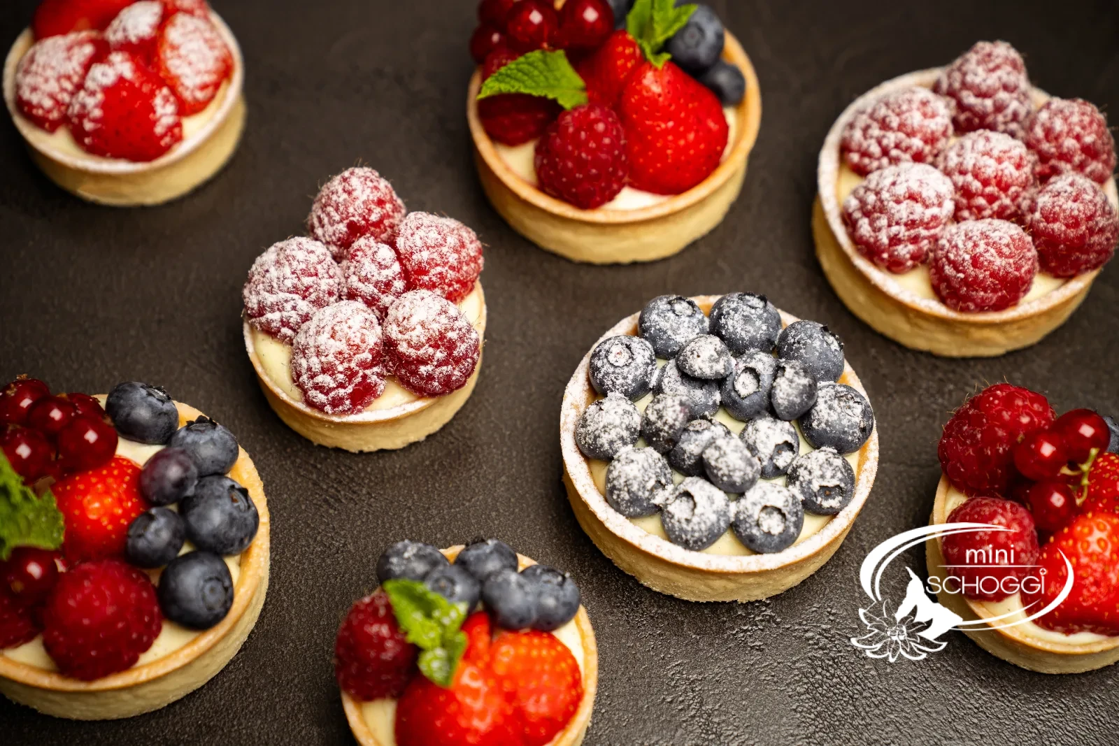 Fertige Vanillecreme-Törtchen mit frischen Beeren und Puderzucker