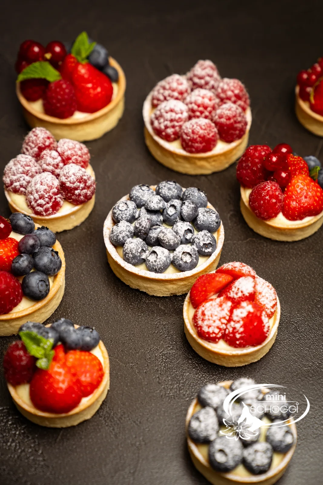 Fertige Vanillecreme-Törtchen mit frischen Beeren und Puderzucker