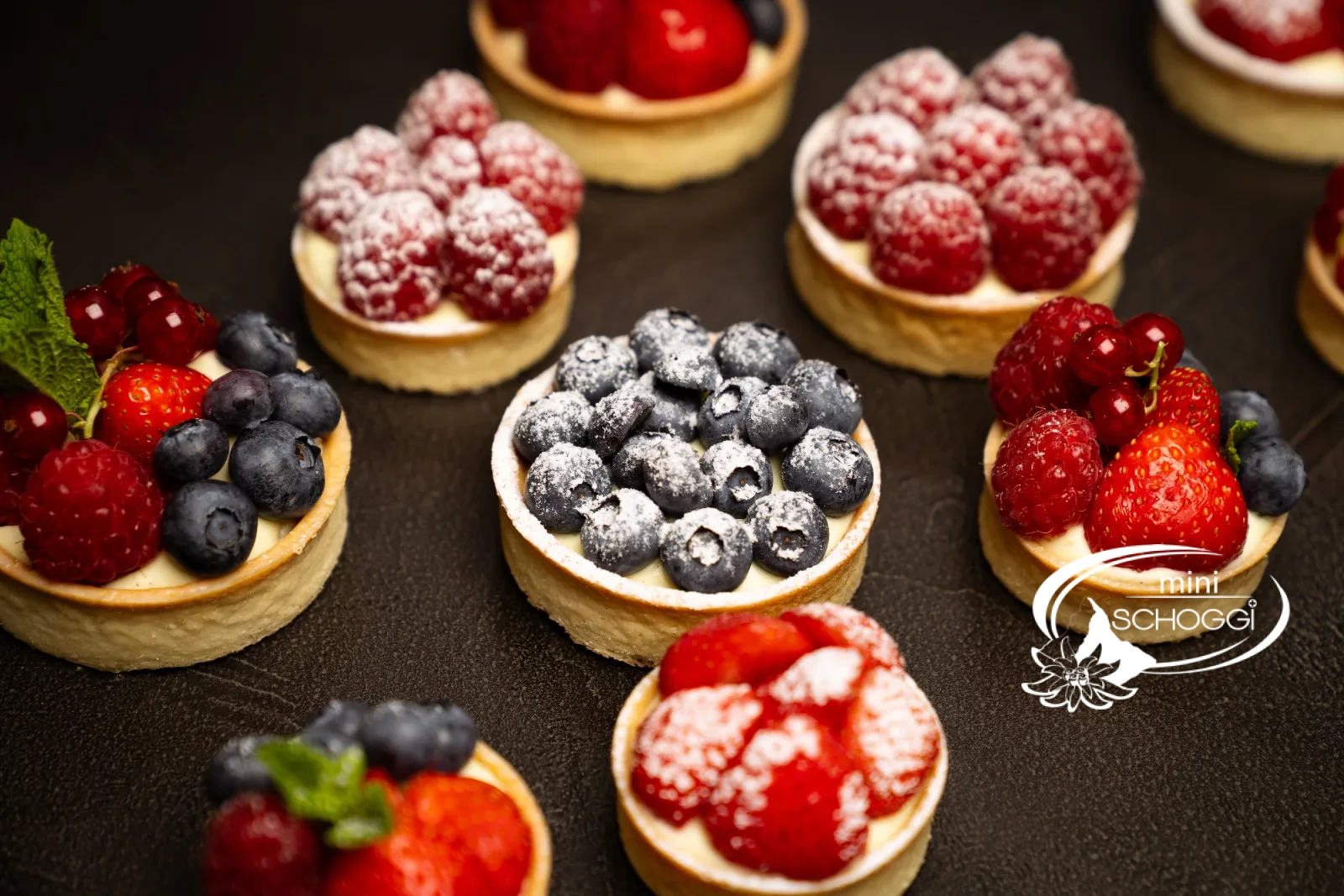 Fertige Vanillecreme-Törtchen mit frischen Beeren und Puderzucker
